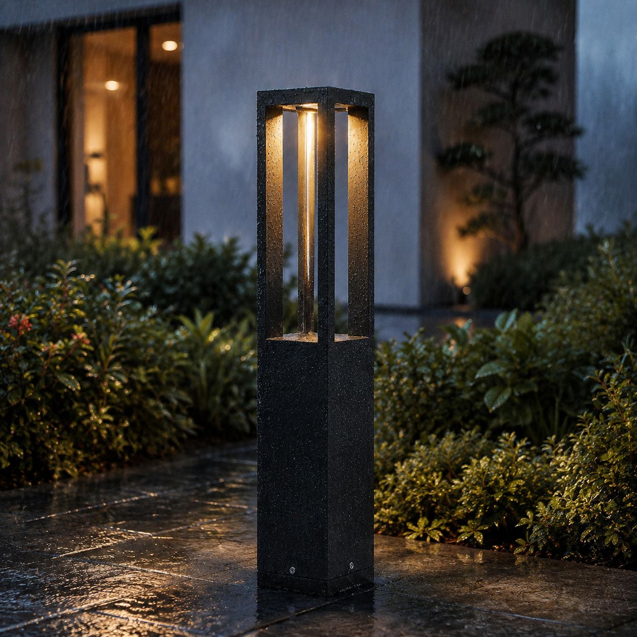 Black aluminium bollard light on a dark plinth beside a modern house at dusk