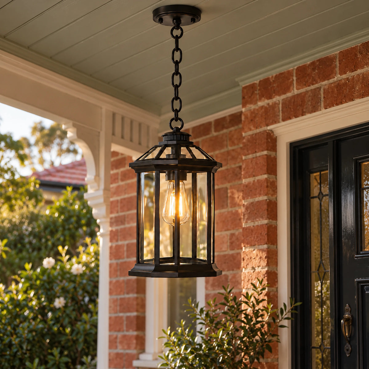 Lit black Portiva glass pendant hanging beneath a painted timber verandah ceiling beside a redbrick entrance.