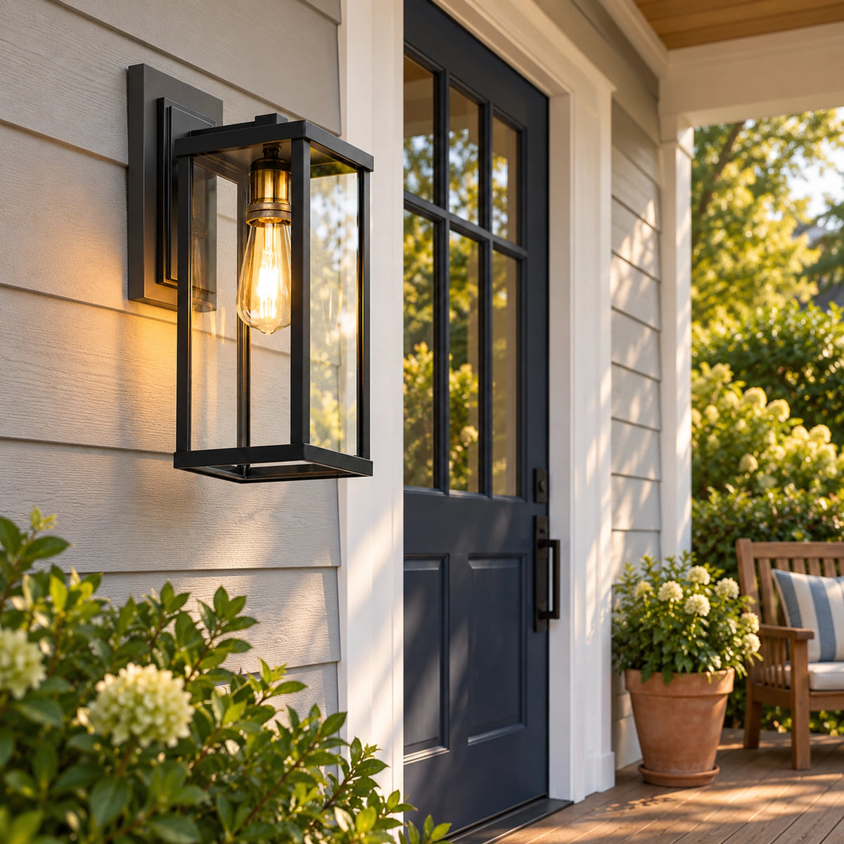 Portelle black glass wall lantern beside a dark front door on a clapboard porch with a timber chair.