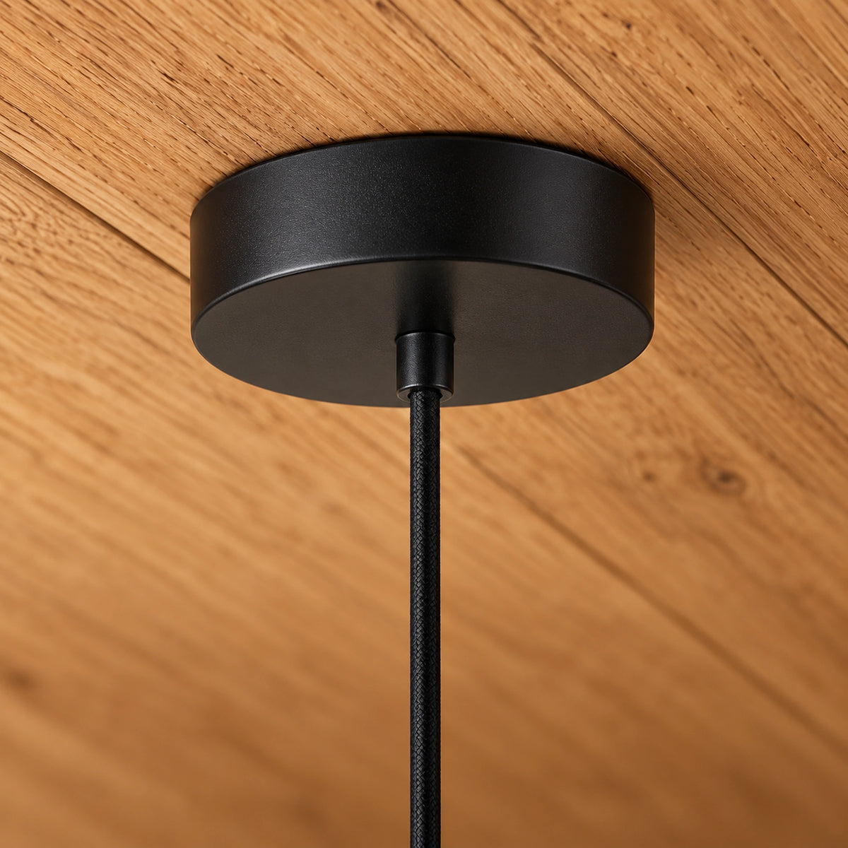 Close-up of Shizora’s black circular ceiling canopy fitted flush to timber, with its cord descending from the centre.