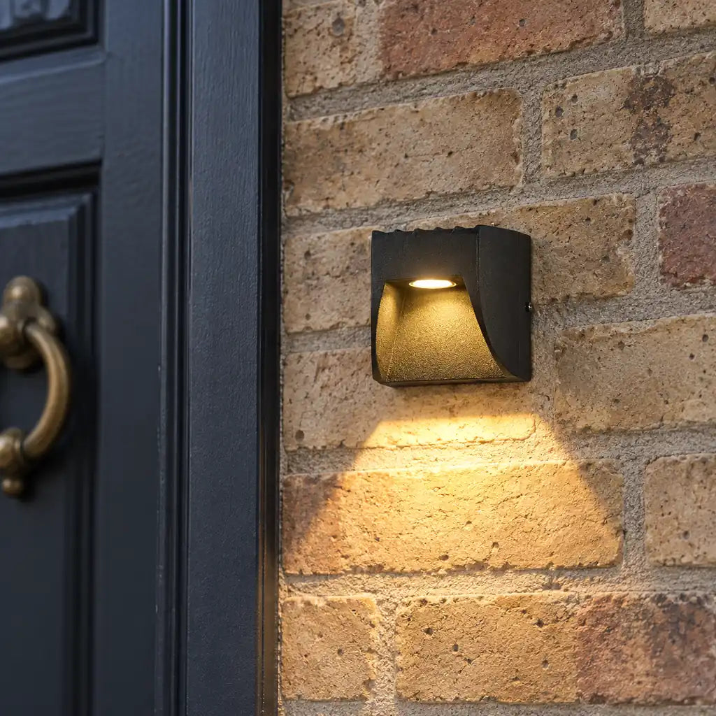 Luminara 9cm black downward wall light beside a charcoal front door on buff brickwork