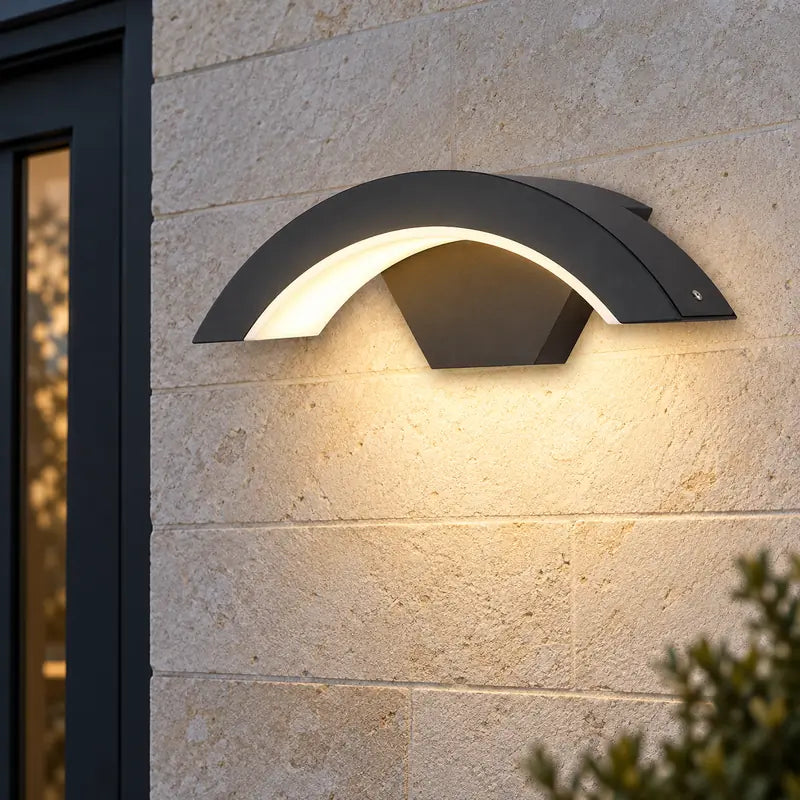 Luminara 18W Warm Light curved black wall sconce beside a stone entrance